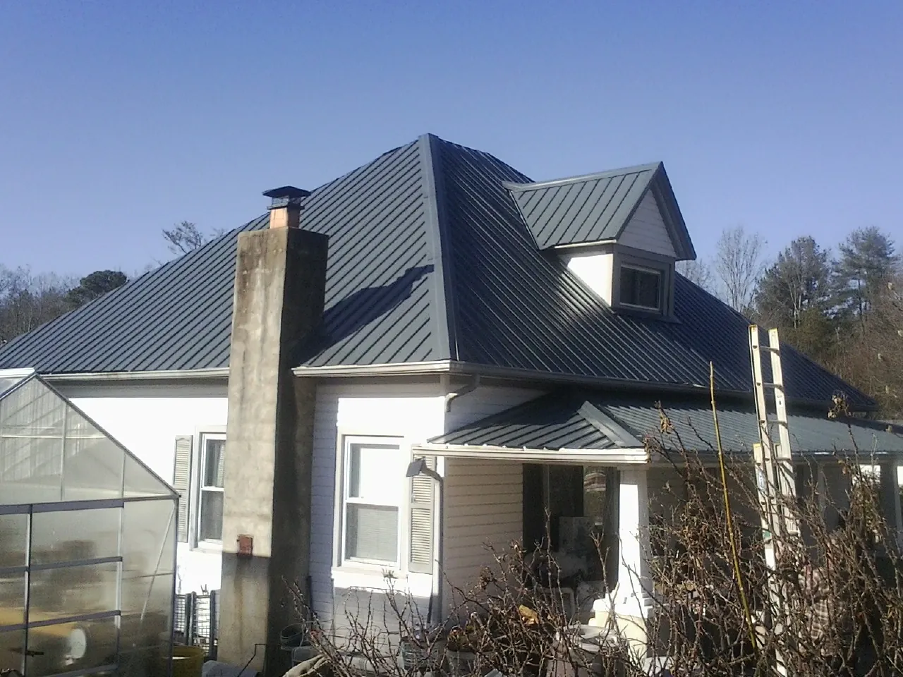 Dark blue standing seam metal roof on a white farmhouse with dormer — Slate & Tile Roof Repair by Roofing Brothers in Mantee