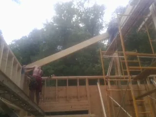 Carpenter raising a rafter beam on a new second story frame in Mantee