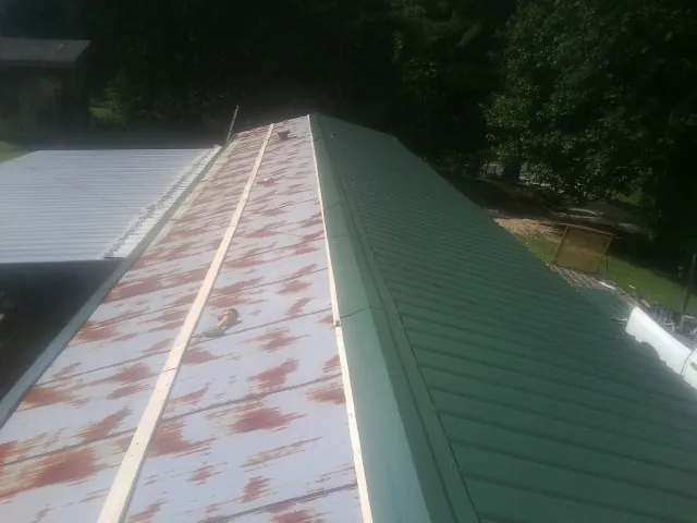 Old rusted panels beside newly installed green metal roofing — Wind Damage Roof Repair by Roofing Brothers in Mantee