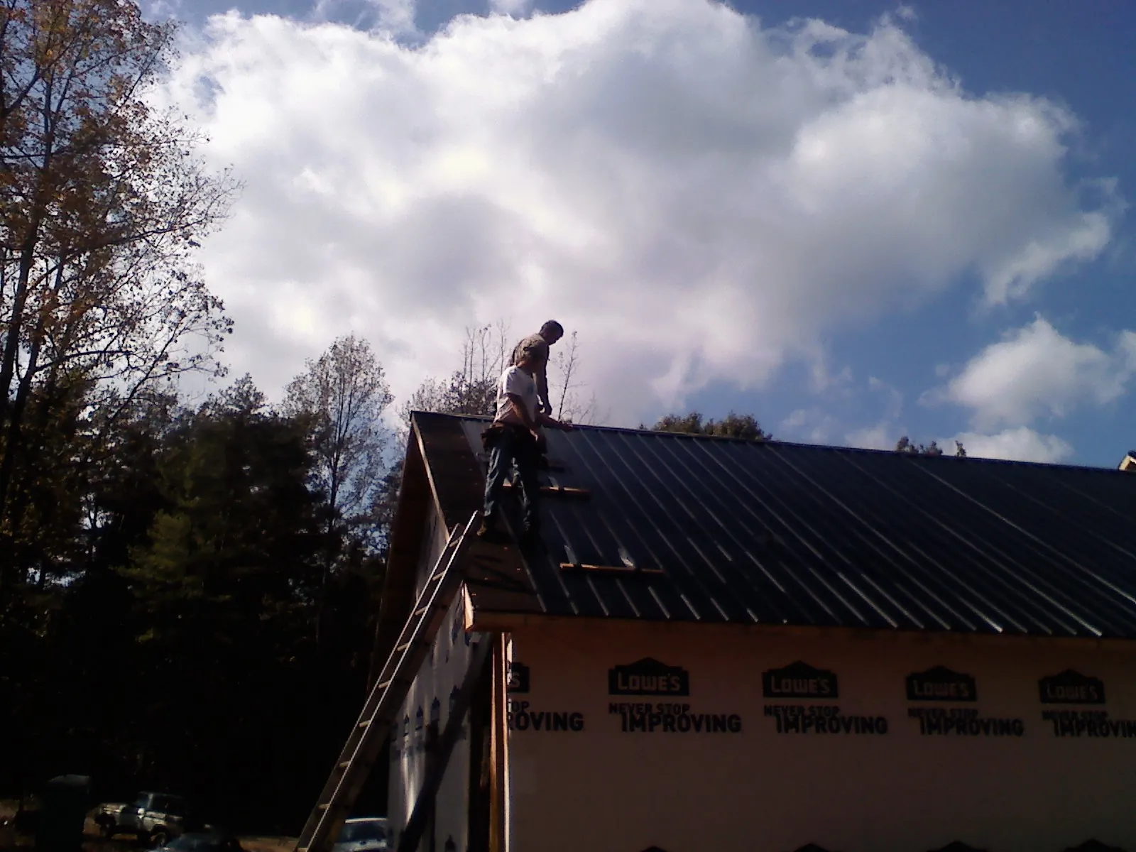 Roofer fastening dark metal panels high against a cloudy sky, from a Roof Inspection job in Mantee